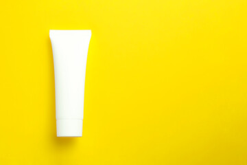 Cosmetic cream in white tube on yellow background with copy space. Skincare mockup concept