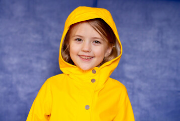 a happy blonde girl in a yellow jacket on a blue background looks at the camera and smiles