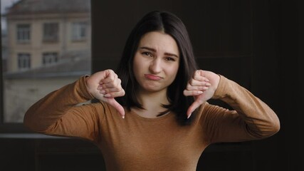 Indoor portrait young emotional girl teenager caucasian millennial woman model brunette showing dislike putting thumb down expressing displeasure disagreement disapproval refusal bad negative attitude - Powered by Adobe