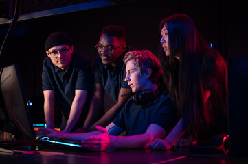 Two guys and a girl in medical masks in a computer club give support to their friend during his game