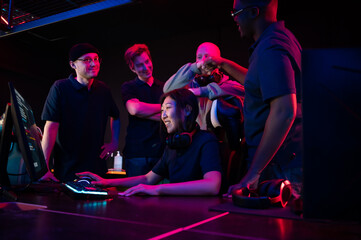 Asian girl playing in a computer club, guys standing behind and prompting