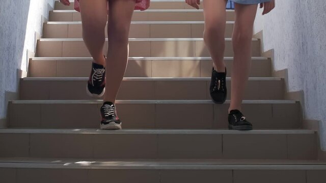 Two girls in short dresses and sports shoes going down the stairs in slow motion.