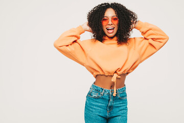 Beautiful black woman with afro curls hairstyle.Smiling model in orange hoodie and trendy jeans...