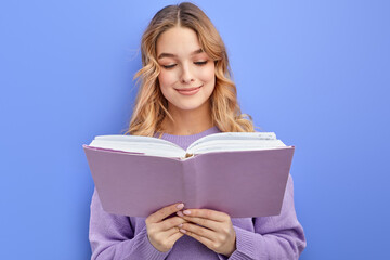 Fototapeta premium smiling teen girl reading book, isolated over blue background