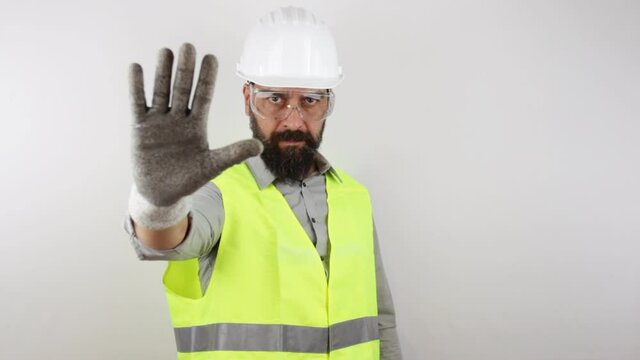 Civil engineer wearing safety glasses and work helmet doing negative stop sign with hand, standing on isolated white background. 