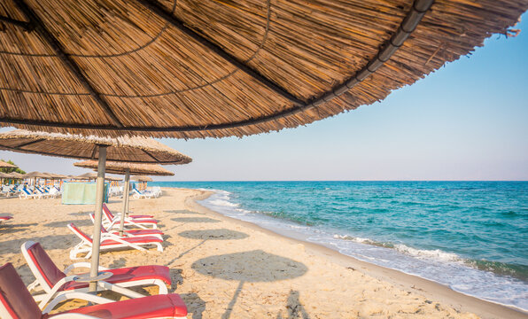 Straw umbrella and sunbeds on Marmari beach, Kos, Greece. Beautiful sandy beach with clear water, no people. Dodecanese islands, Aegean Sea.