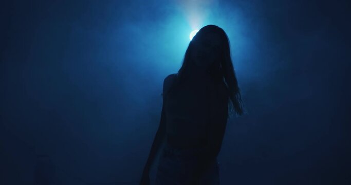 Mysterious female silhouette in blue light and smoke cloud at night. 4k video of young girl in haze