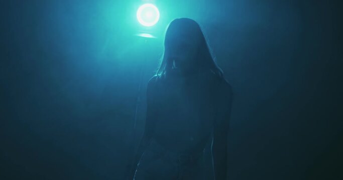 4k video of dancing girl in haze. Mysterious moving female silhouette in smoke cloud and blue light.