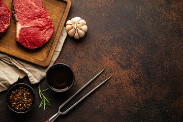 Cooking background for menu or template with raw meat steaks on wooden cutting board, spices and olive oil on rustic stone background with space for text 