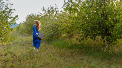 A woman in a blue dress runs through the rows of green trees. Blonde hair develops from movement. High quality photo