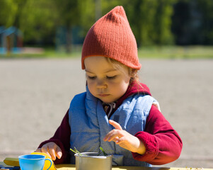 Little girl play with set of children's toy colorful dishes, cones and chestnutson on the bench. Kid toy utensil for girls game. Early spring