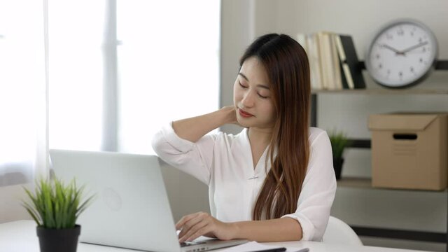 Young asian business woman rubbing her shoulder she's has shoulder, neck pain and hurt get stressed be tired from working with laptop a long time she symptom office syndrome.