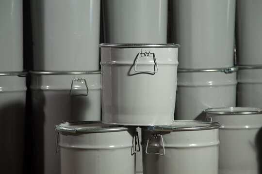 There are many round barrels in white and blue at the production site. The barrels contain oil and chemical products.