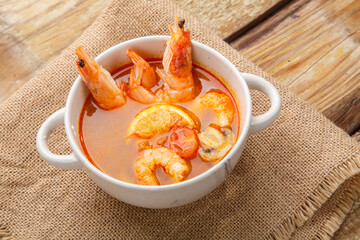 Tom yam soup with shrimps in a tureen on burlap on a wooden table.