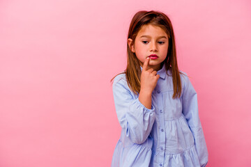 Little caucasian girl isolated on pink background  looking sideways with doubtful and skeptical...