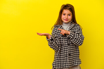 Little caucasian girl isolated on yellow background excited holding a copy space on palm.
