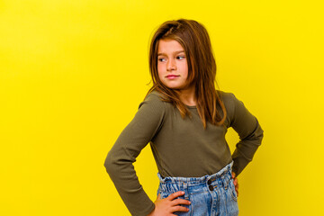 Little caucasian girl isolated on yellow background looks aside smiling, cheerful and pleasant.