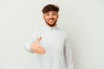Young Moroccan man wearing a typical arab clothes isolated on white background stretching hand at camera in greeting gesture.