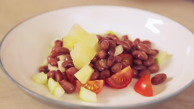 A woman's hand with a spoon puts the pineapple pieces into a plate of salad