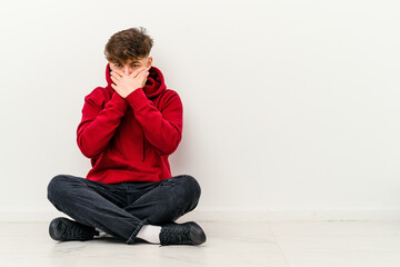 Young Moroccan man sitting on the floor isolated on white background covering mouth with hands looking worried.