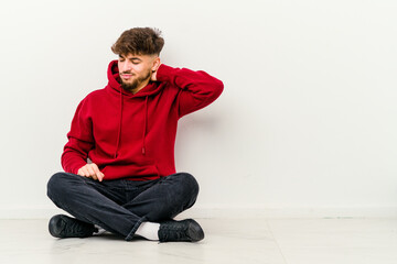 Young Moroccan man sitting on the floor isolated on white background having a neck pain due to stress, massaging and touching it with hand.