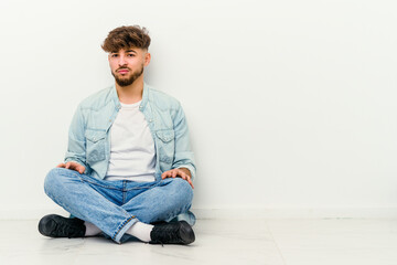 Young Moroccan man sitting on the floor isolated on white background sad, serious face, feeling miserable and displeased.