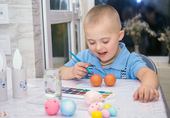 A boy with Down syndrome draws, a genetically ill child paints Easter eggs, preparation for Easter,...