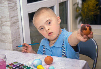 A boy with Down syndrome draws, a genetically ill child paints Easter eggs, preparation for Easter,...
