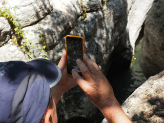 A man holds a phone in his hands and takes a photo surrounded by canyons and a river.