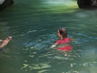 A girl poses for the camera swimming in a turquoise river of a rocky gorge