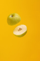Green apple, cut in half, levitating, on a yellow background