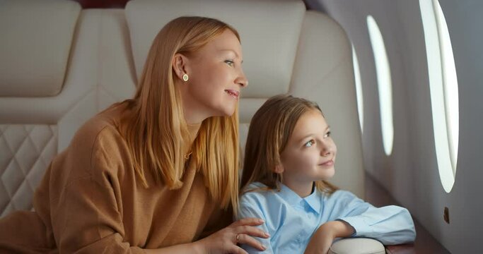 Mature elegant mother and preteen daughter looking through window flying on airplane