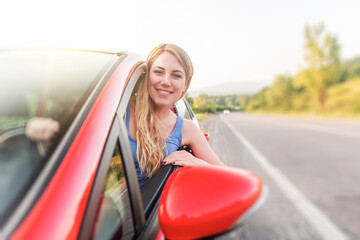 Happy beautiful woman is driving a red car.