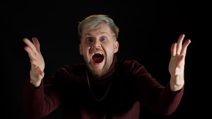 Stylish young man with blue eyes shout loudly, wins competition achieves goal, makes triumph gesture, guy says yes feels like winner shows fist, happy dream come true on black studio background