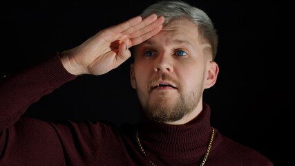 Obraz premium Facial expression of trendy bearded guy with gray hair. Close up view of handsome man in stylish blouse looks around with his hand on his forehead, waving hand hi hello welcome bye on black background