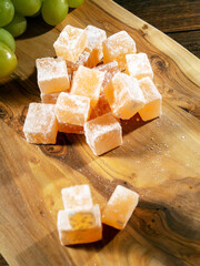 Traditional Turkish and Greek rose flavor jelly candy in sugar powder and green grapes on a wooden board and black background. Arabic style confectionery. Still life