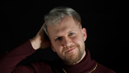 Cheerful smiling young man in trendy stylish clothes holding hand over head, looking at camera on black background. Fashion people sincere emotions. Attractive guy studio shot. Fun and enjoyment
