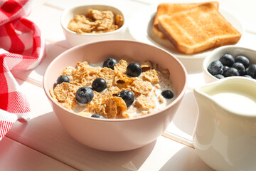 Healthy breakfast of whole wheat flakes with milk, blueberries and toast close-up on wooden table. Selective focus