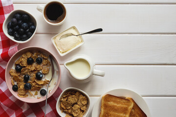 Healthy breakfast of whole wheat flakes with milk, blueberries, cup of coffee and toast on wooden table with copy space. Top view, flat lay