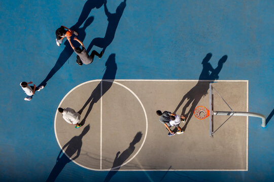 young man playing basketball at dusk or morning light with long shadows high angle bird's eye view