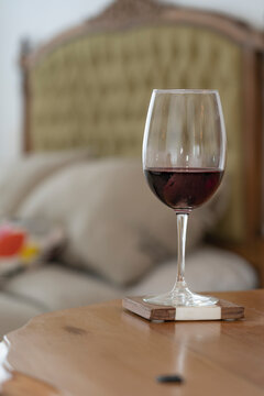 Glass of red wine on a table, behind a bed with a stylish back, and window. Day time. Room place.