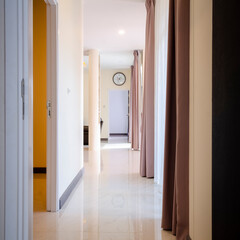 Square photo the interior of a new home long corridor with doors and brown tone curtains,  Decorated with a white clock.