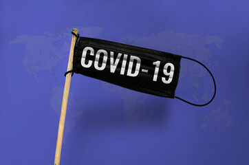 The medical mask Waving black flag on pole with text COVID-19. Black mask on blue the world map textured background. Black virus Attack flag. Concept of coronavirus COVID