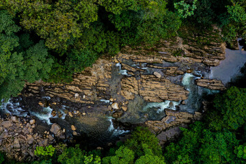 Aerial top view of a river going through a rock bed that is worn out from the water and surrounded by trees