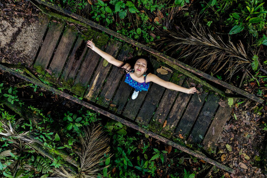 A woman standing on a wooden bridge inside a forest with arm stretched and eyes closed enjoying nature