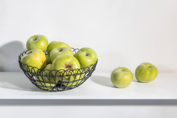 Vase with green apples on the white table.