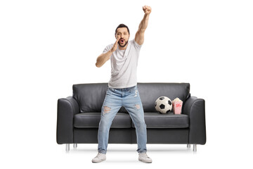 Young male football fan watching a match in front of a couch and shouting
