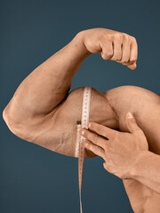 Muscular male bodybuilder with a measuring tape measures his biceps. Isolated on dark blue background.