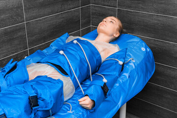 Young beautiful girl lies on a couch in a suit of pressotherapy and lymphatic drainage massage.