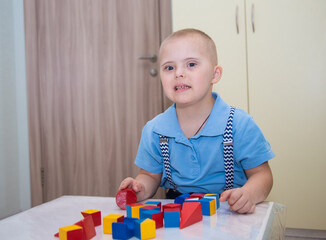 A boy with Down syndrome plays a construction set, a genetically ill disabled child builds a tower...
